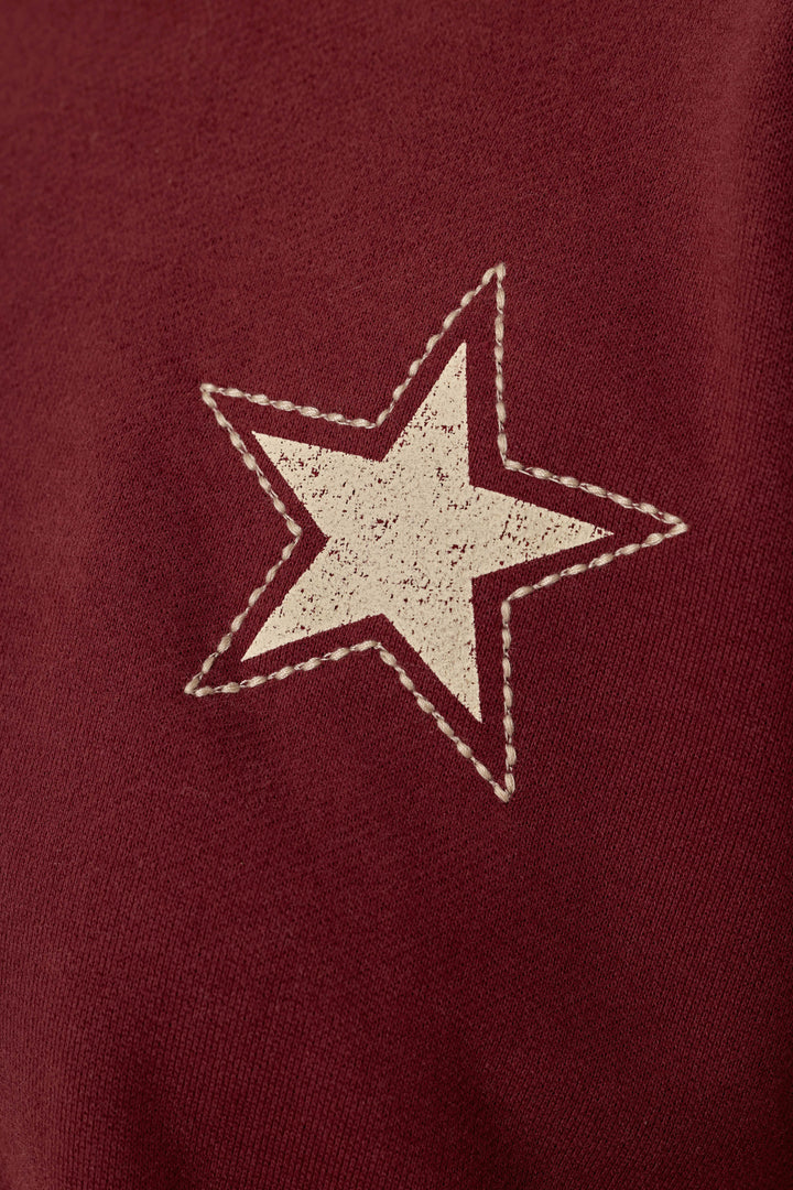 The P.J. Salvage Western Ways Dark Wine Simone Sweatshirt features a slightly distressed white star with a stitched border printed on a maroon background, giving it a vintage-inspired look.