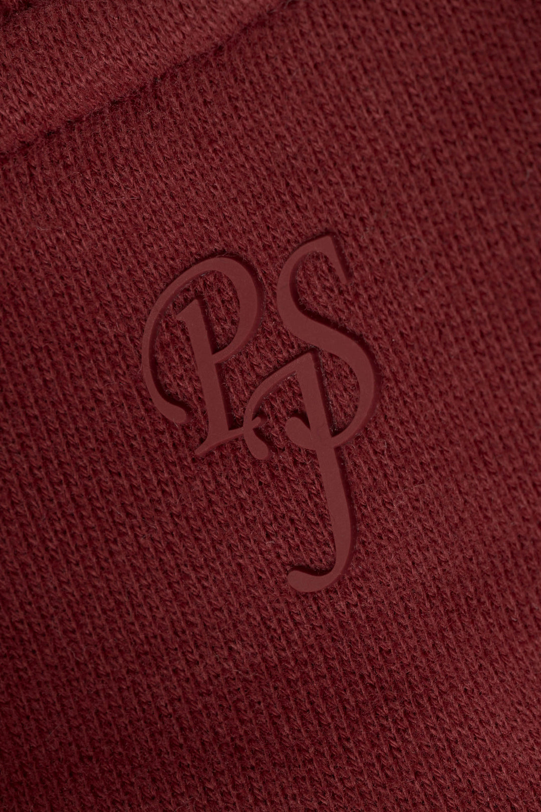 Close-up of textured dark wine fabric featuring embossed overlapping “PS” letters in a stylized serif font.