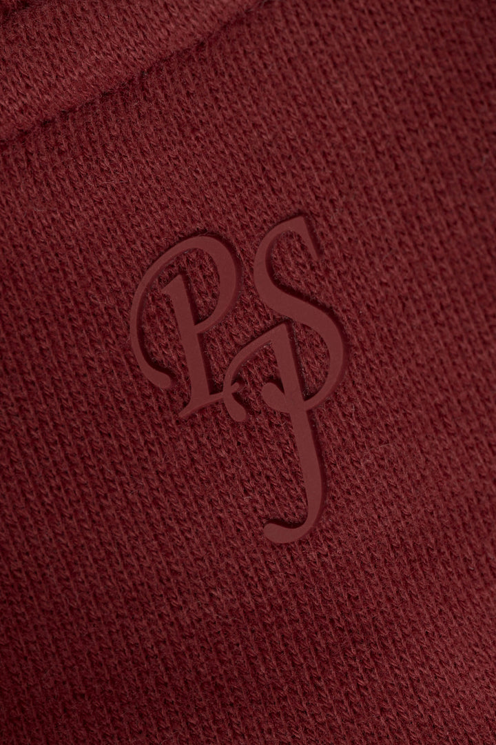 Close-up of textured dark wine fabric featuring embossed overlapping “PS” letters in a stylized serif font.