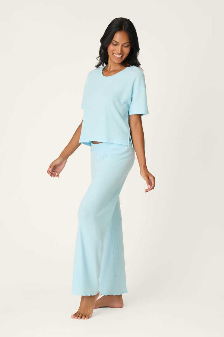 A woman with long dark hair smiles while wearing the P.J. Salvage Weekend Waffles Crystal Blue Long PJ Set, standing barefoot against a light background and posing casually, perfectly capturing relaxed loungewear style.