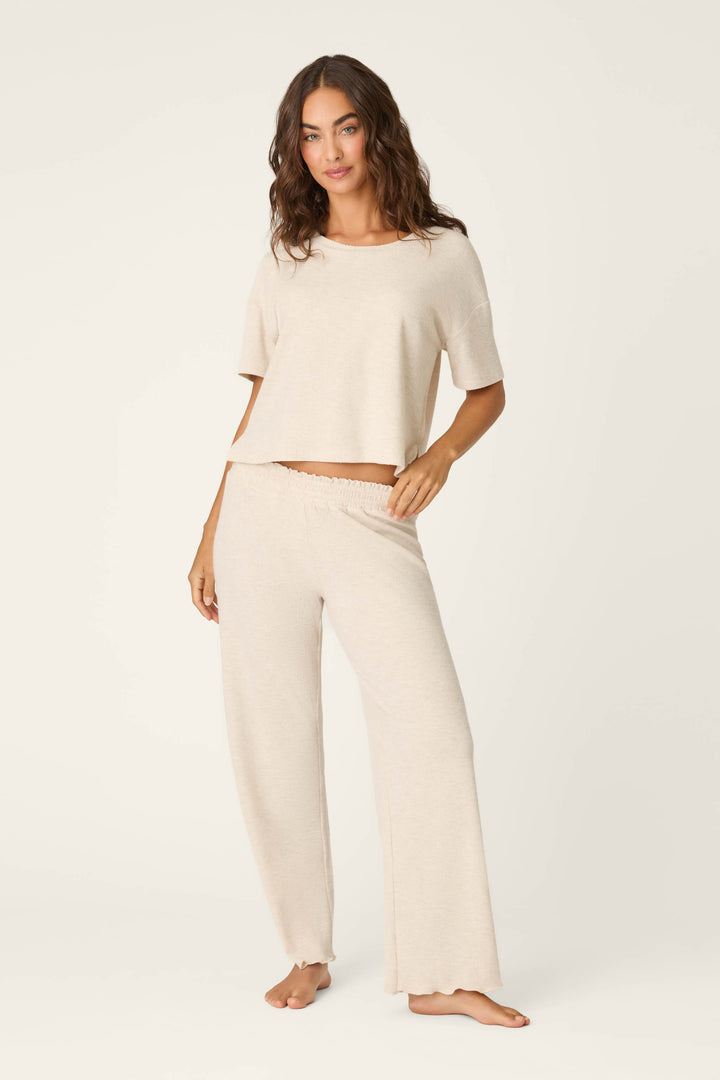 A woman with wavy brown hair poses barefoot against a plain backdrop, wearing P.J. Salvage’s Weekend Waffles Light Oatmeal Long PJ Set, showcasing the soft waffle fabric and the relaxed comfort perfect for cozy nights at home.