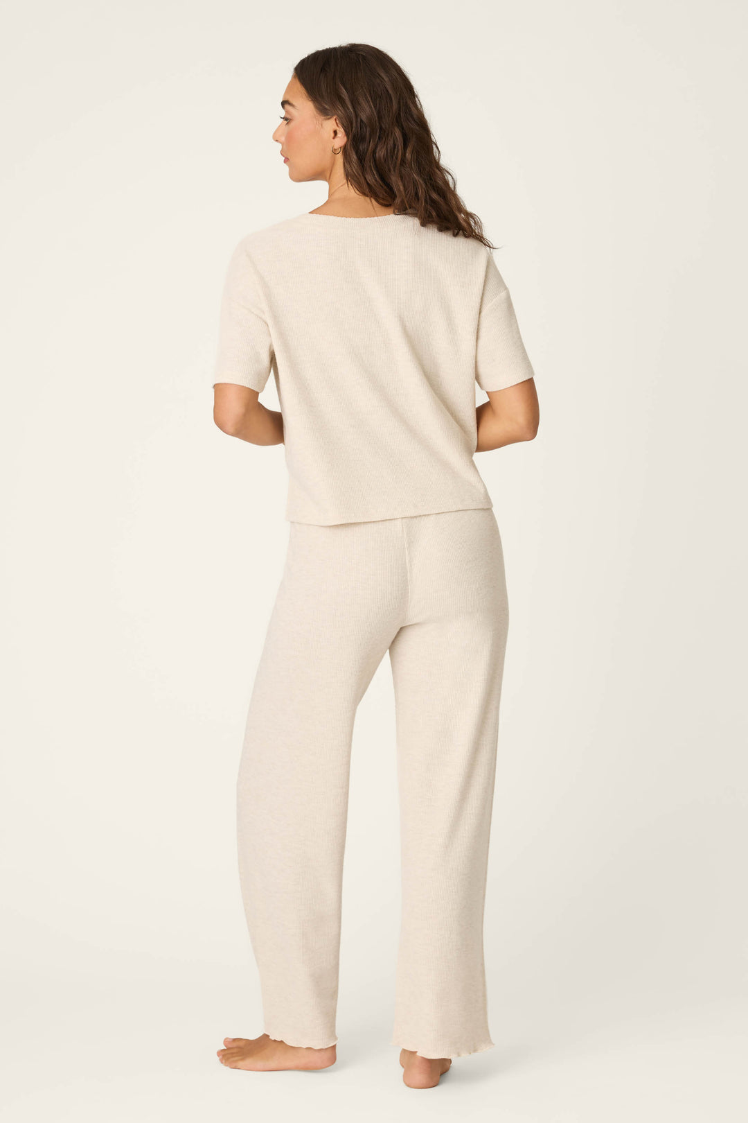 A woman stands barefoot, facing away, wearing the P.J. Salvage Weekend Waffles Light Oatmeal Long PJ Set—a matching short-sleeve top and wide-leg pants—in front of a plain off-white background.