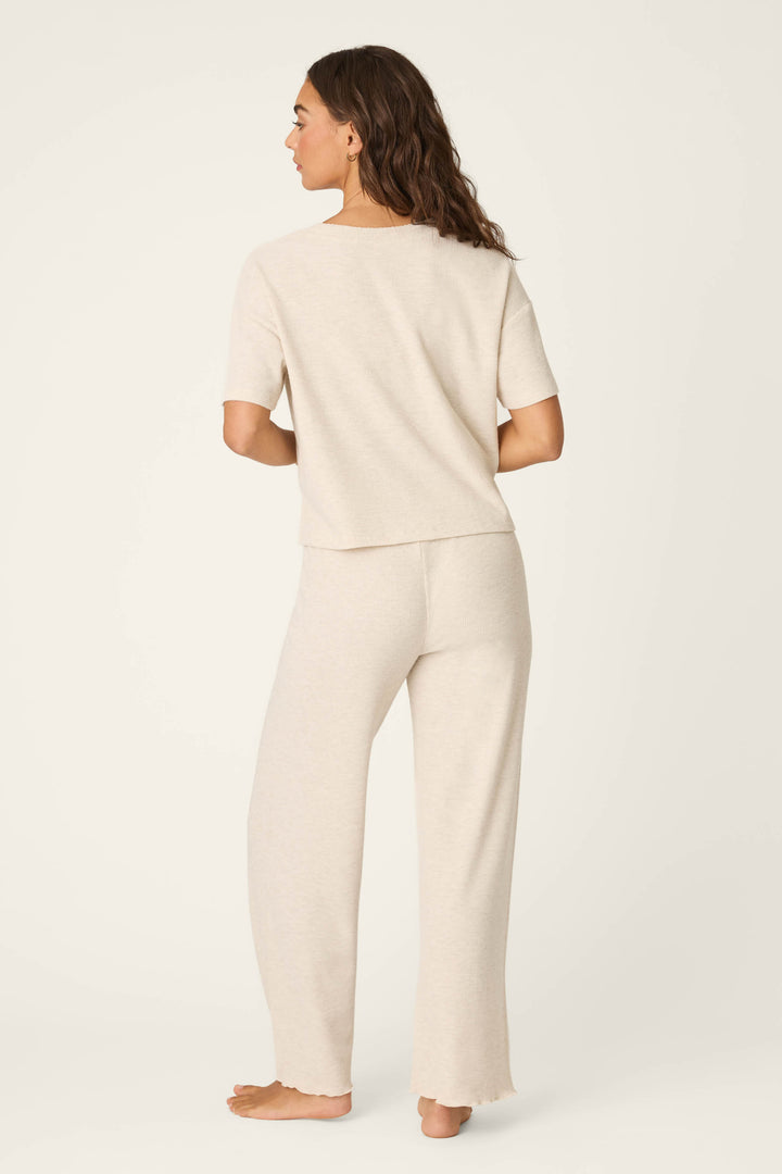 A woman stands barefoot, facing away, wearing the P.J. Salvage Weekend Waffles Light Oatmeal Long PJ Set—a matching short-sleeve top and wide-leg pants—in front of a plain off-white background.
