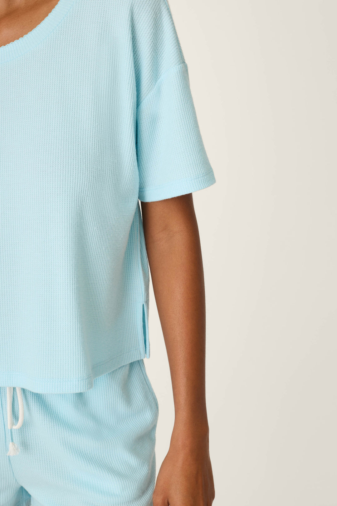 Wearing the P.J. Salvage Weekend Waffles Crystal Blue Short Sleeve Top, a person is shown from shoulders to mid-thigh against a plain background, with only the left side of their body visible.