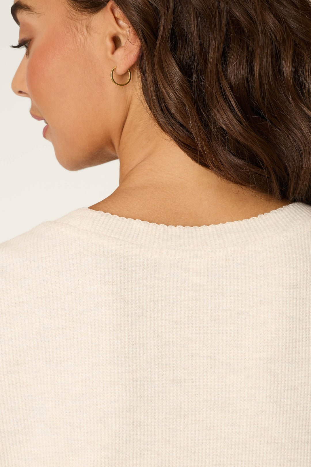 Close-up of a woman with wavy brown hair wearing a gold hoop earring and the P.J. Salvage Weekend Waffles Light Oatmeal Short Sleeve Top, featuring a round neckline and waffle fabric. Part of her face is seen in profile against a light background.