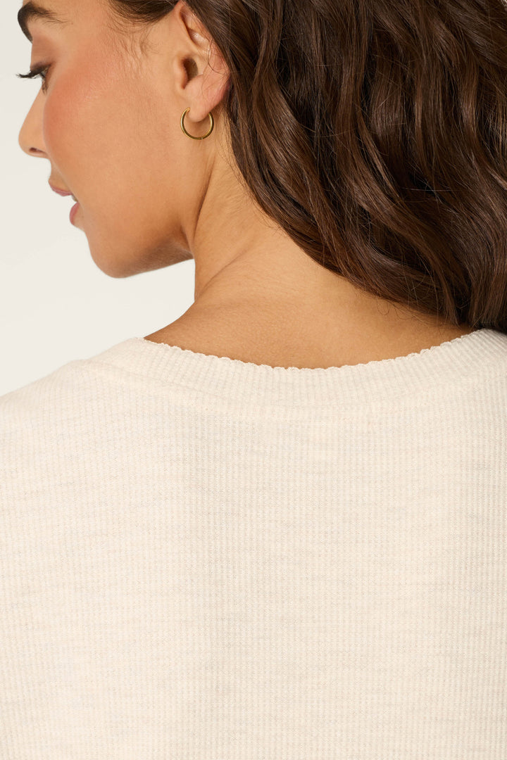 Close-up of a woman with wavy brown hair wearing a gold hoop earring and the P.J. Salvage Weekend Waffles Light Oatmeal Short Sleeve Top, featuring a round neckline and waffle fabric. Part of her face is seen in profile against a light background.