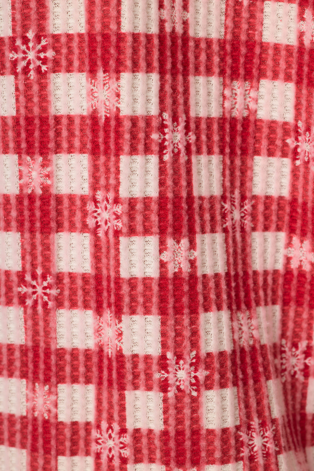 A close-up of a red and white gingham print on a waffle texture fabric, with white snowflakes throughout.