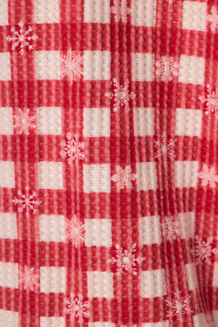 A close-up of a red and white gingham print on a waffle texture fabric, with white snowflakes throughout.