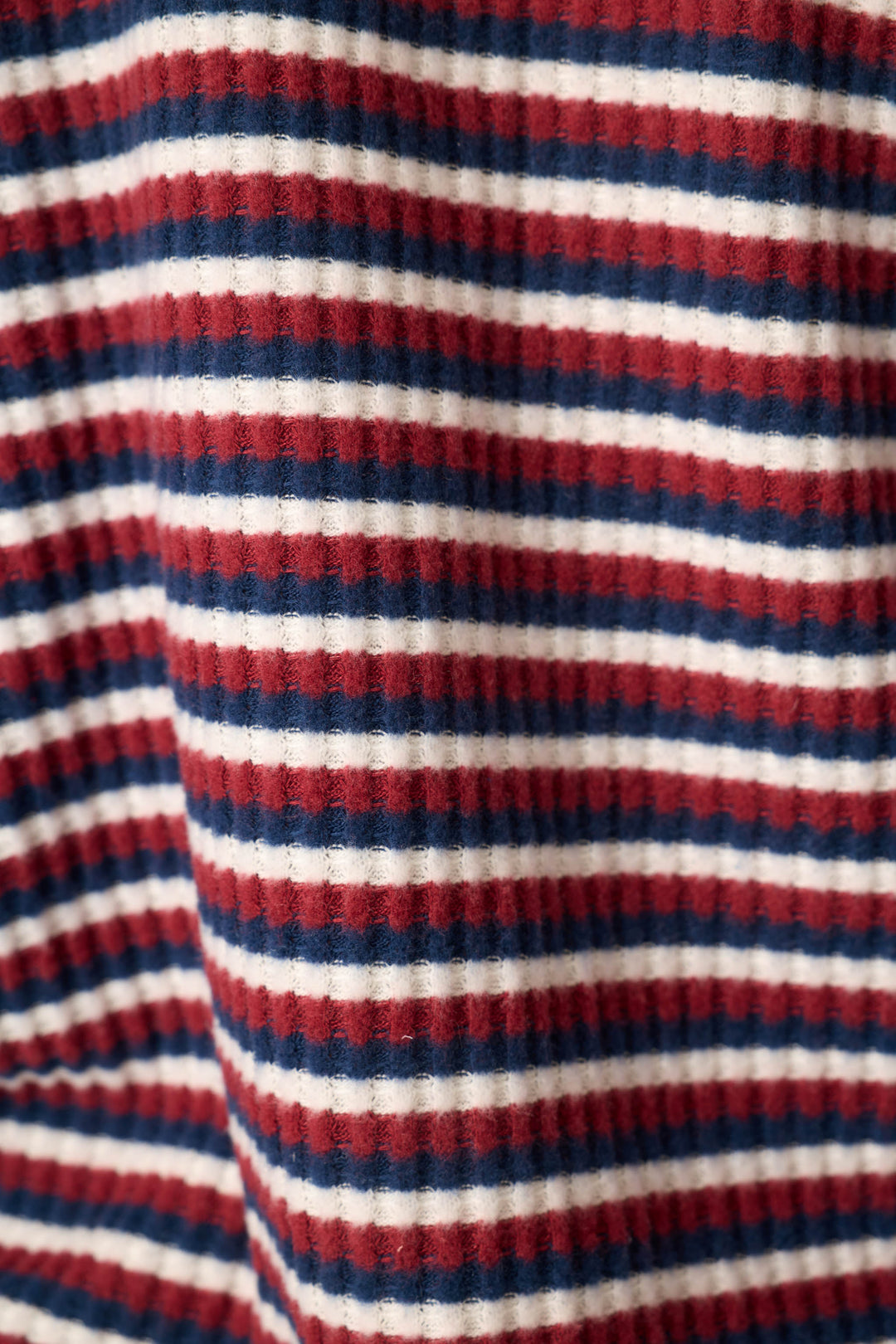A close-up of a ribbed knit fabric with horizontal stripes in red, navy blue, and white.