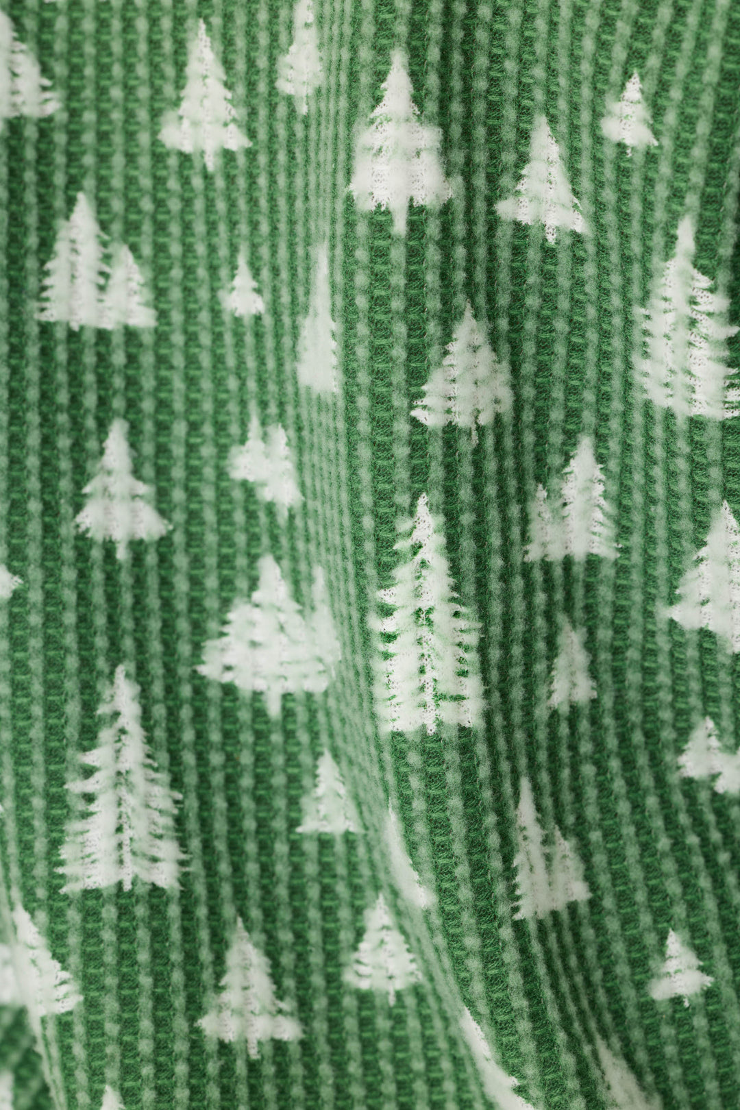 A close-up of a green ribbed knit fabric with a repeating white Christmas tree pattern.