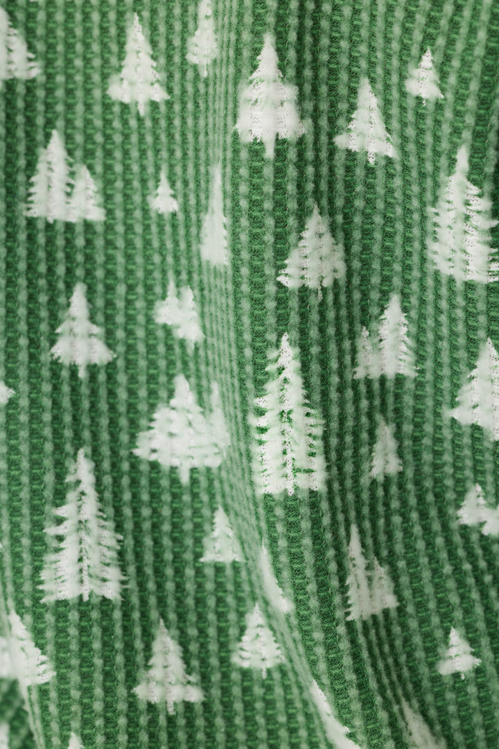 A close-up of a green ribbed knit fabric with a repeating white Christmas tree pattern.