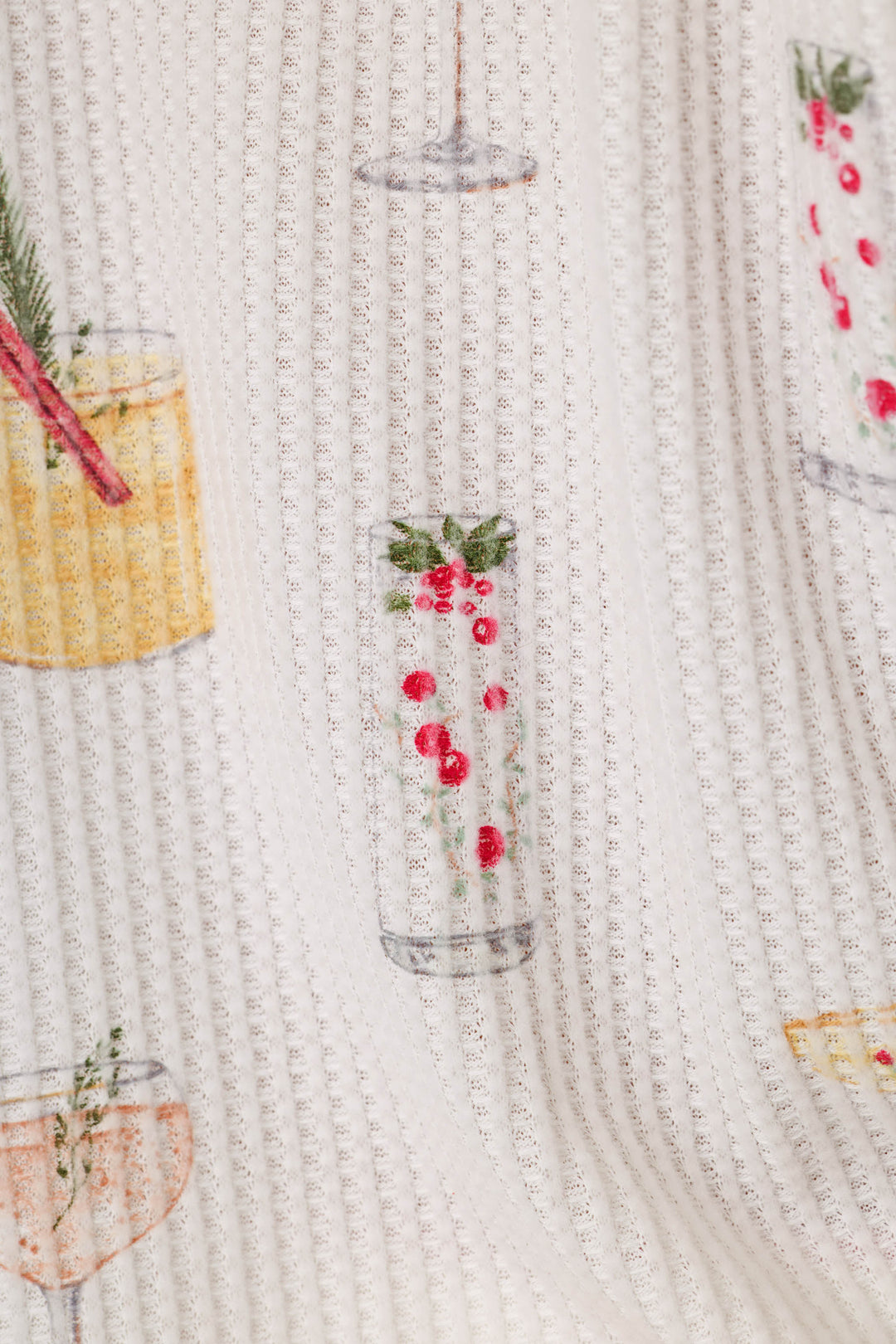 Close-up of a waffle-weave fabric with a repeating pattern of colorful cocktails with festive accents, on a cream background.