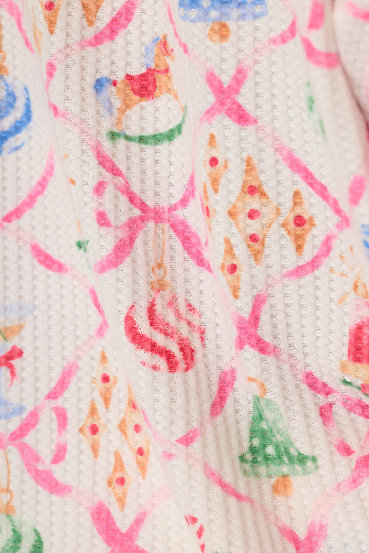 A close-up of a textured waffle-knit fabric featuring a colorful Christmas-themed pattern with pink bows, ornaments, and small holiday illustrations on an off-white background.
