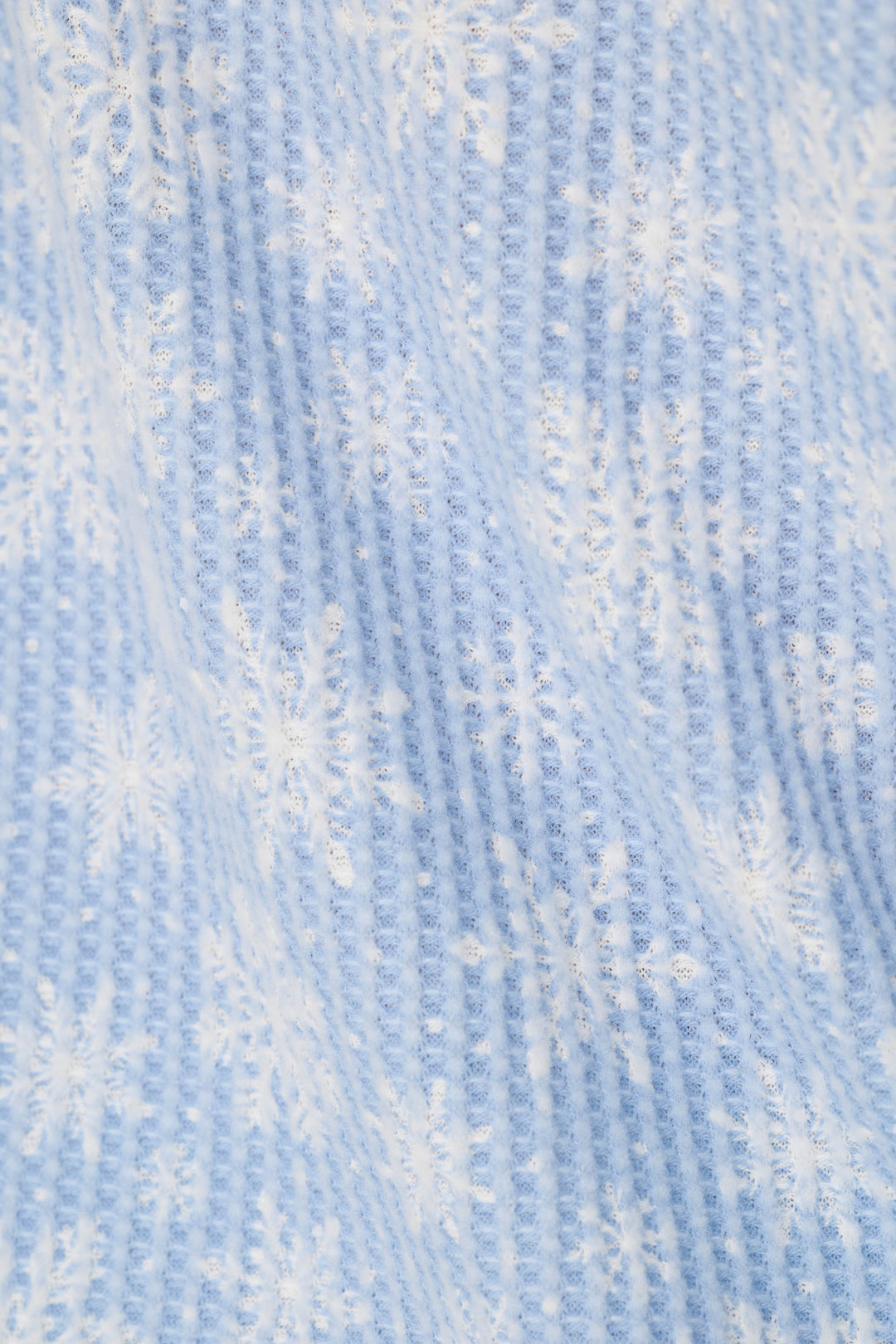 A close-up of a light blue, waffle knit fabric with a white snowflake pattern.