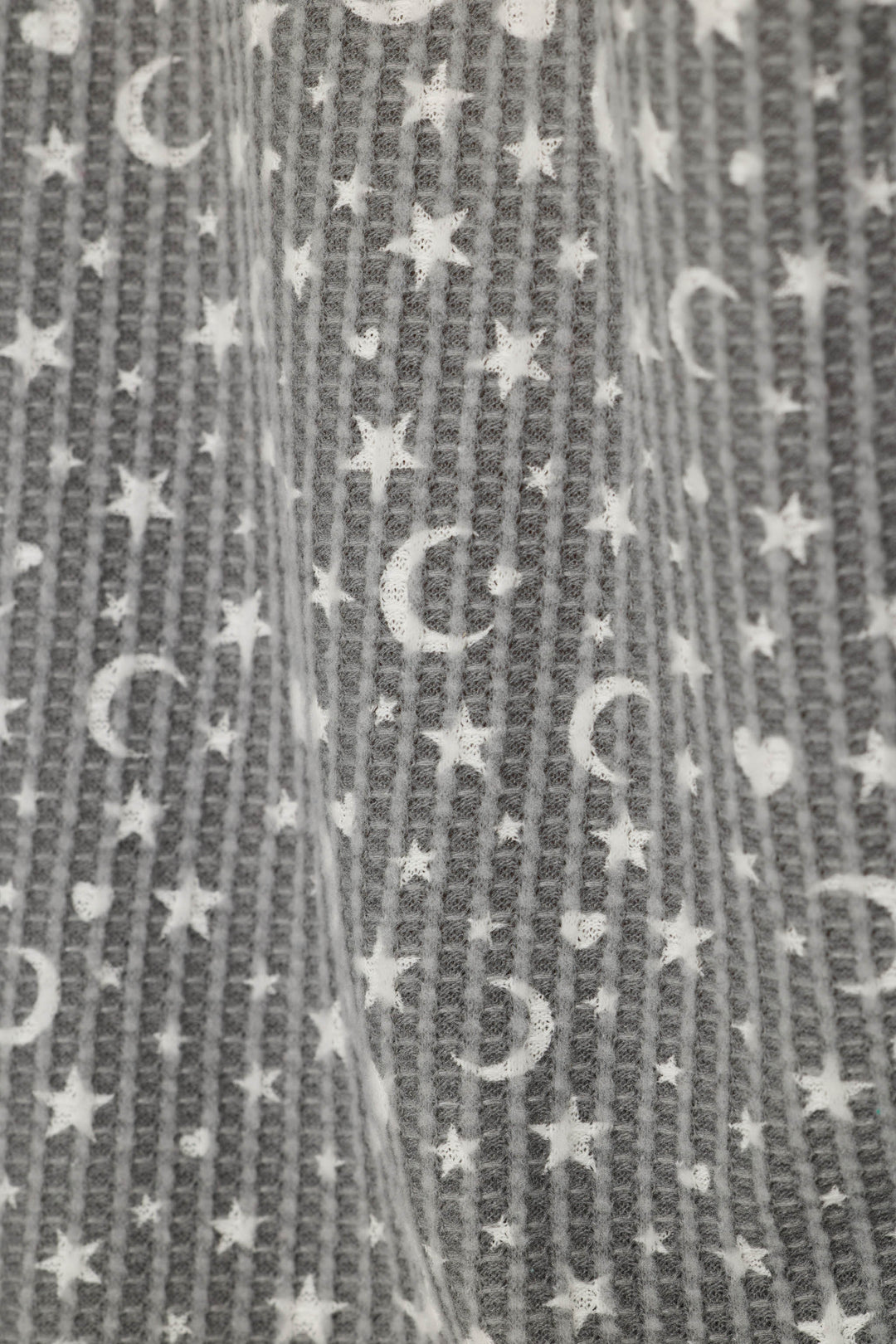 Close-up of a gray waffle textured fabric with a white celestial pattern of stars and crescent moons.