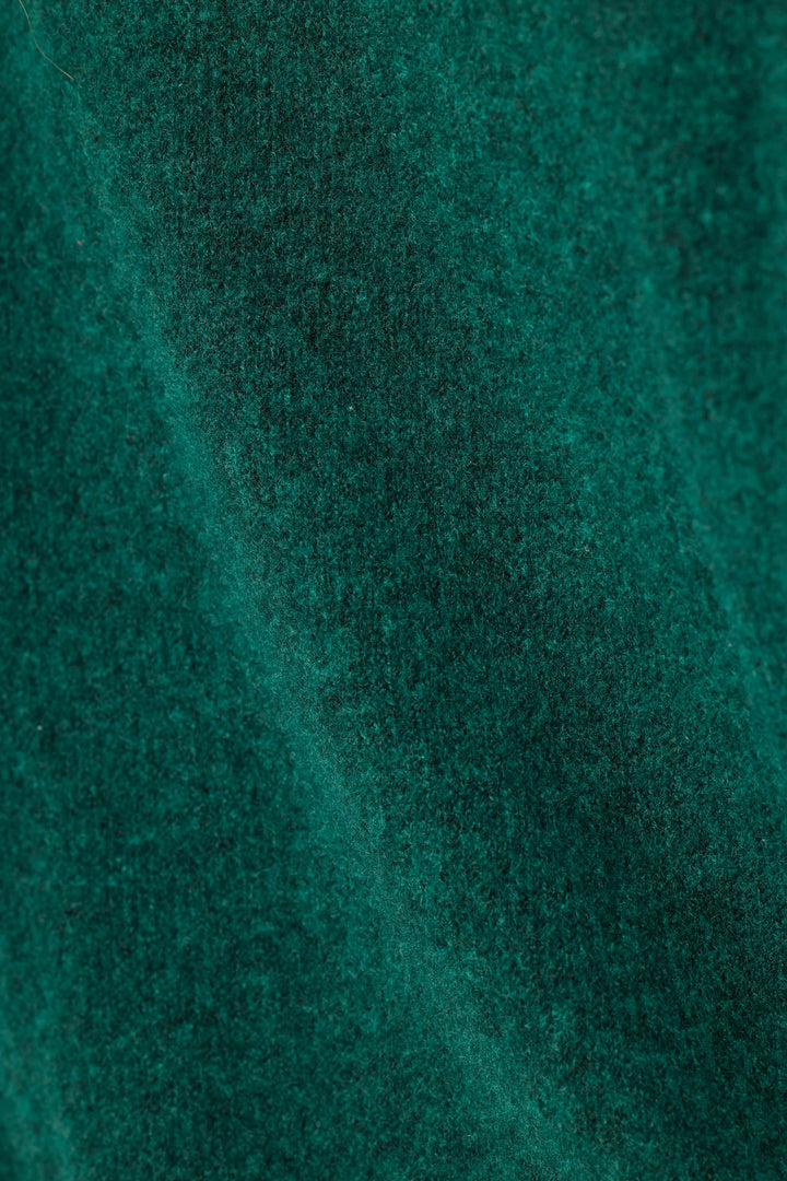 A close-up of dark teal green sweater textured fabric with soft folds and a fine woven surface.