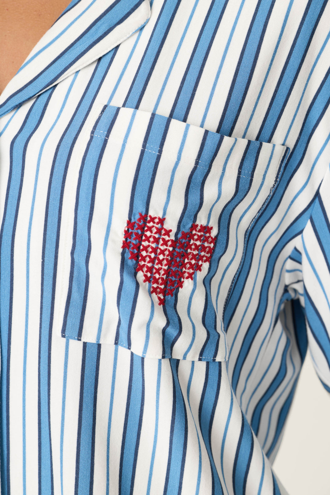 A close-up of the Soiree Dreams Blue Stripe fabric, highlighting the detail of the embroidered red heart on the chest pocket, which is made from several small embroidered X's.