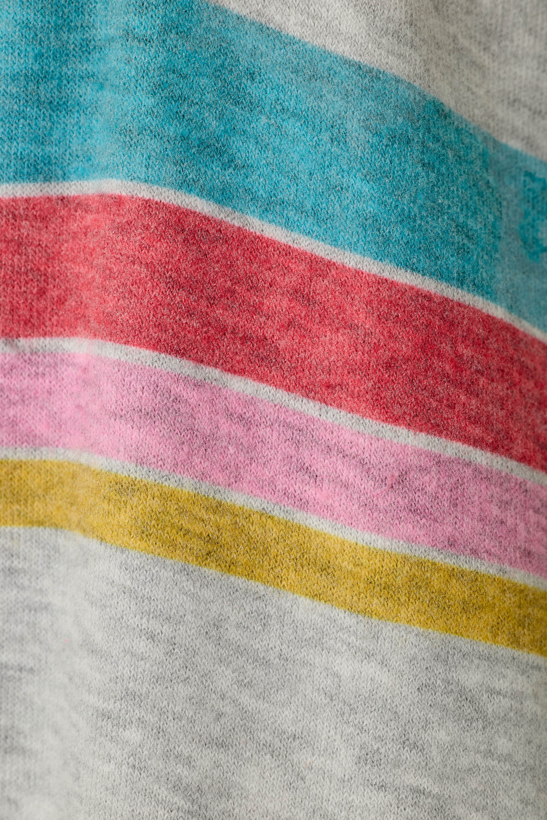 Close-up of a knit fabric featuring horizontal bands of turquoise blue, red, pink, and mustard yellow on a light heather gray background.