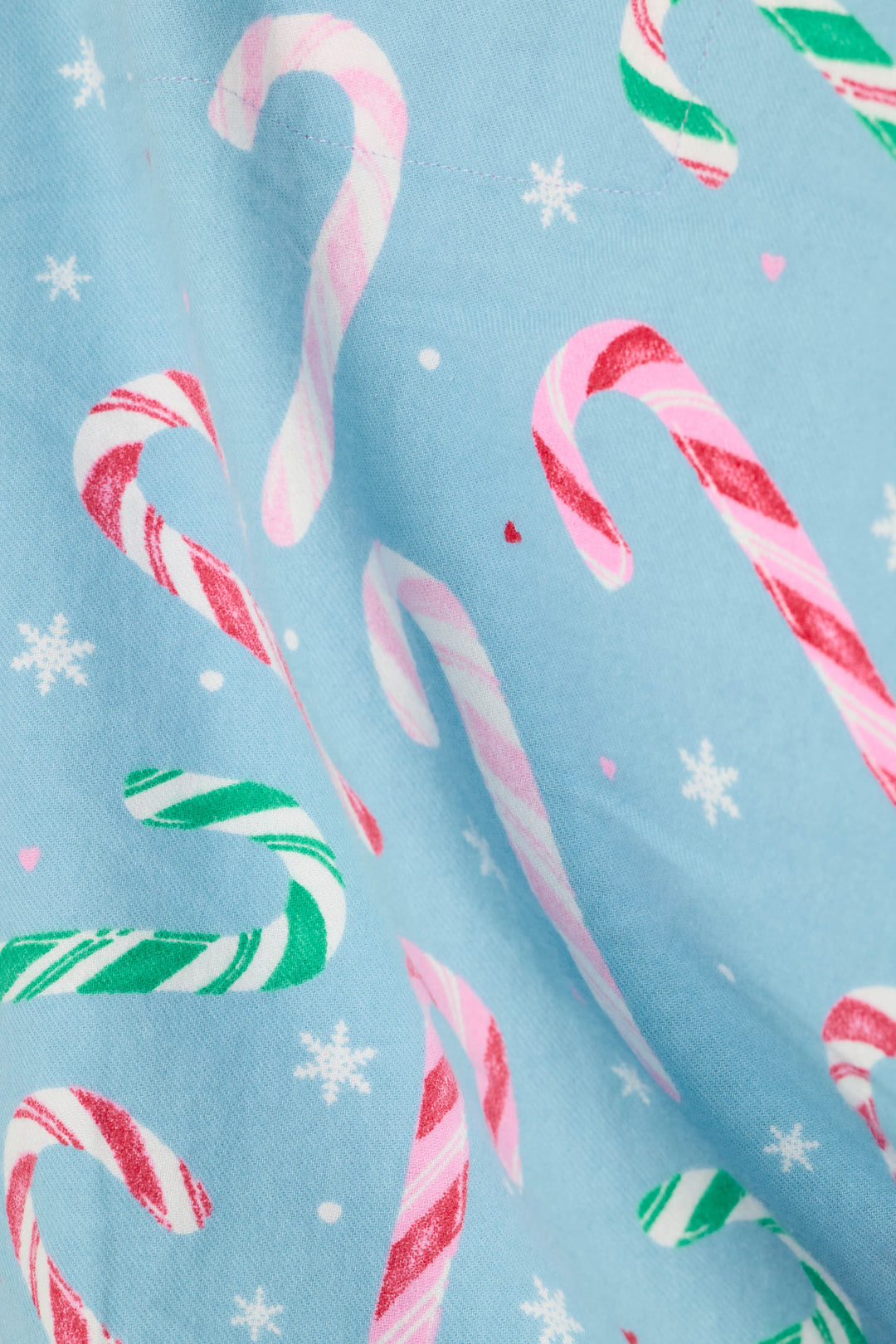 A close-up of light blue fabric printed with candy canes, snowflakes, and small hearts in pink and red.