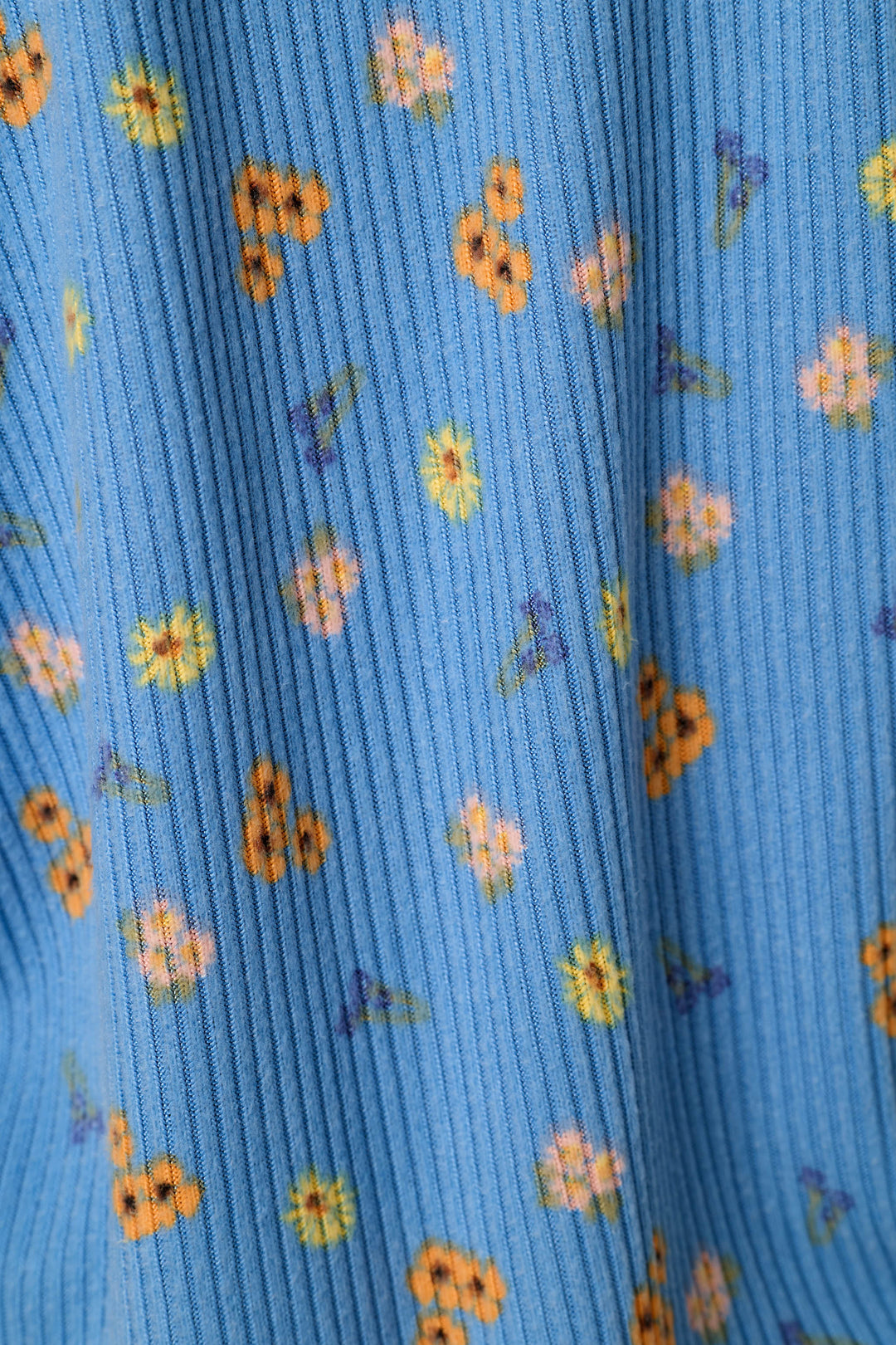 A close-up of a blue ribbed knit fabric with a small-scale floral pattern in yellow, orange, and purple.