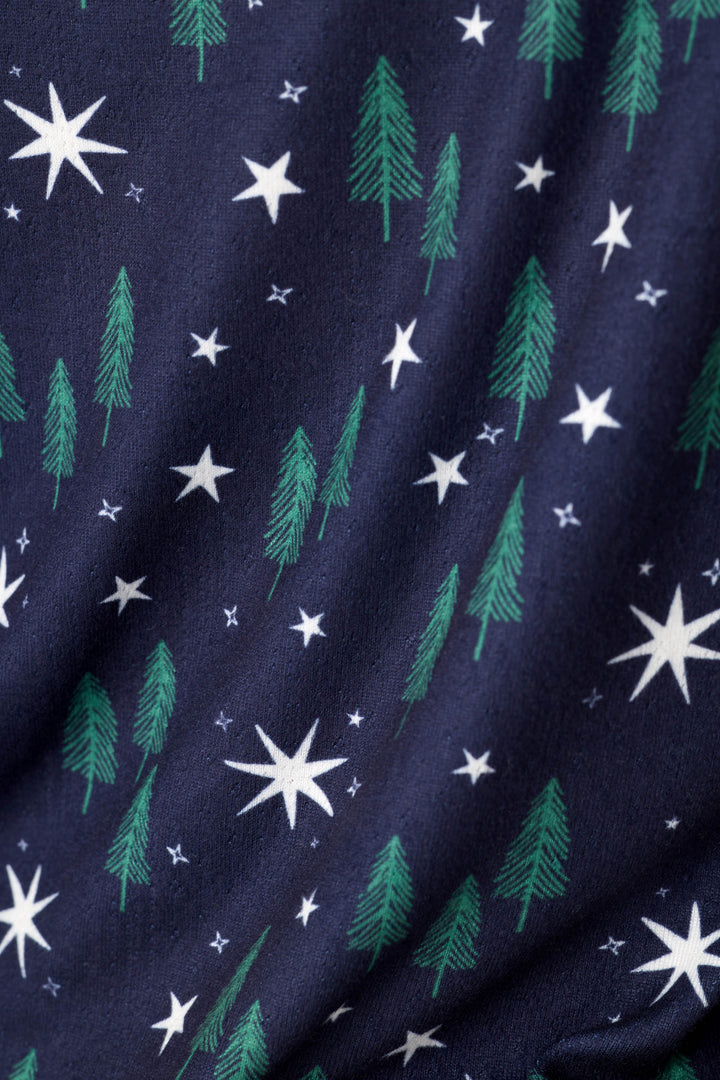 A close-up of navy blue fabric with a repeating pattern of green pine trees and white stars of varying sizes.