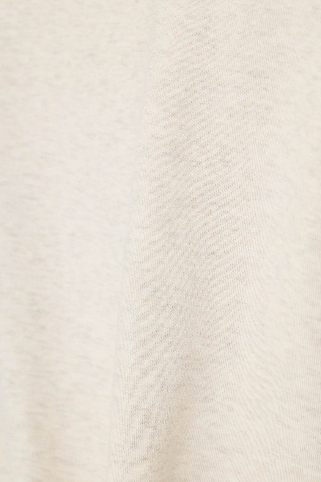 A close-up of a light cream or off-white textured fabric surface with subtle heathering and soft folds.