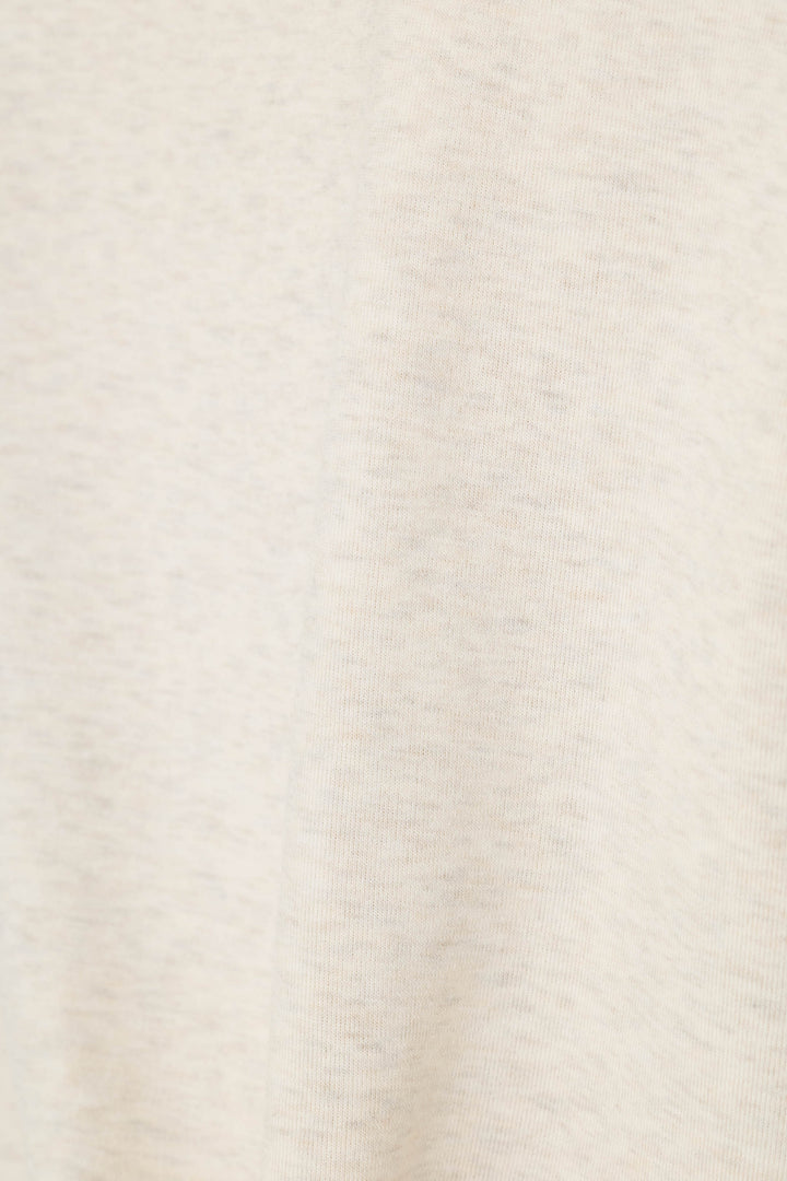 A close-up of a light cream or off-white textured fabric surface with subtle heathering and soft folds.