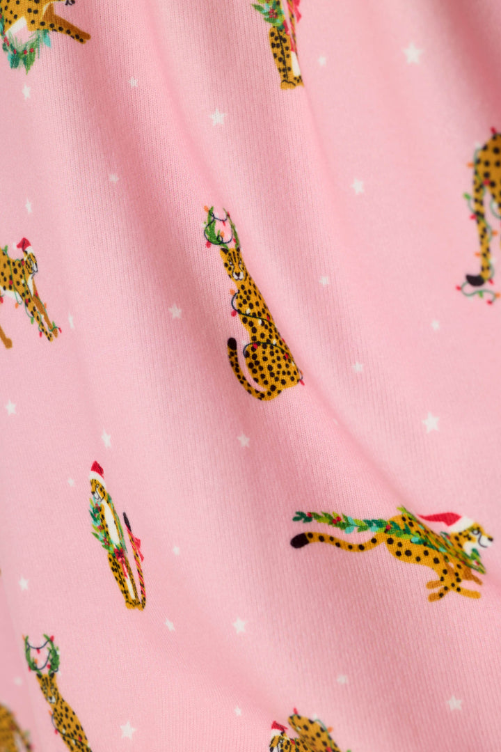 Pink fabric with a repeating print of yellow spotted cheetahs wearing green Christmas wreaths and red Santa hats, interspersed with small white stars.
