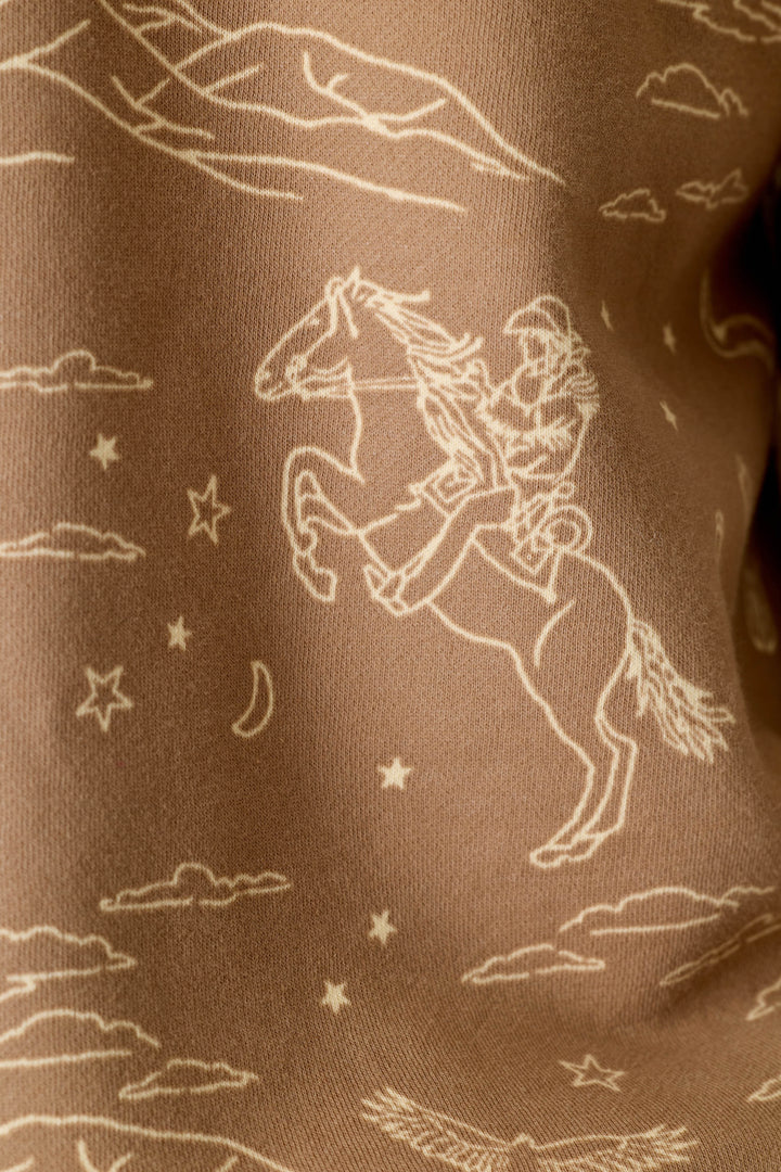 The P.J. Salvage Western Ways Ride ’Em Cowgirl Roll Back Short Sleeve Sweatshirt features a line drawing of a cowgirl on a rearing horse, surrounded by clouds, stars, and a crescent moon, printed on brown fabric.