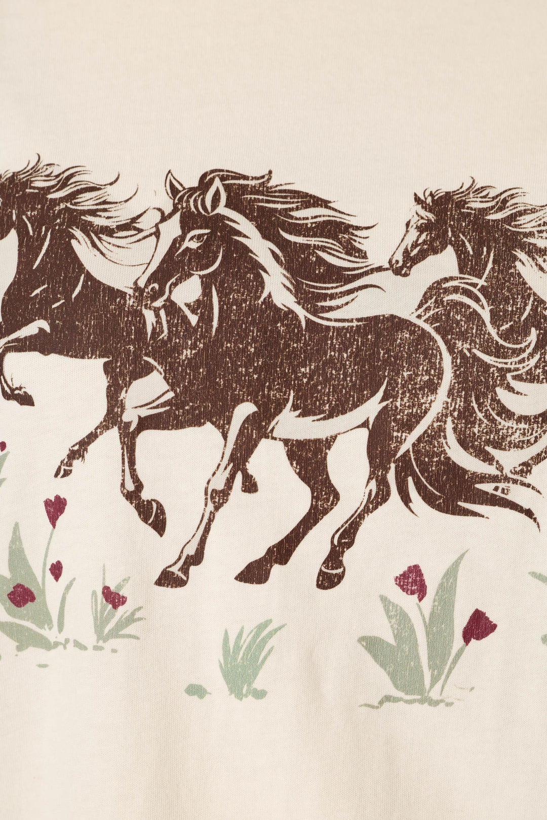 Introducing the P.J. Salvage Western Ways Wild Horses Graphic Shuggie T-Shirt, featuring an illustration of three brown horses with flowing manes running through green grass dotted with small red flowers, all set against a beige background.
