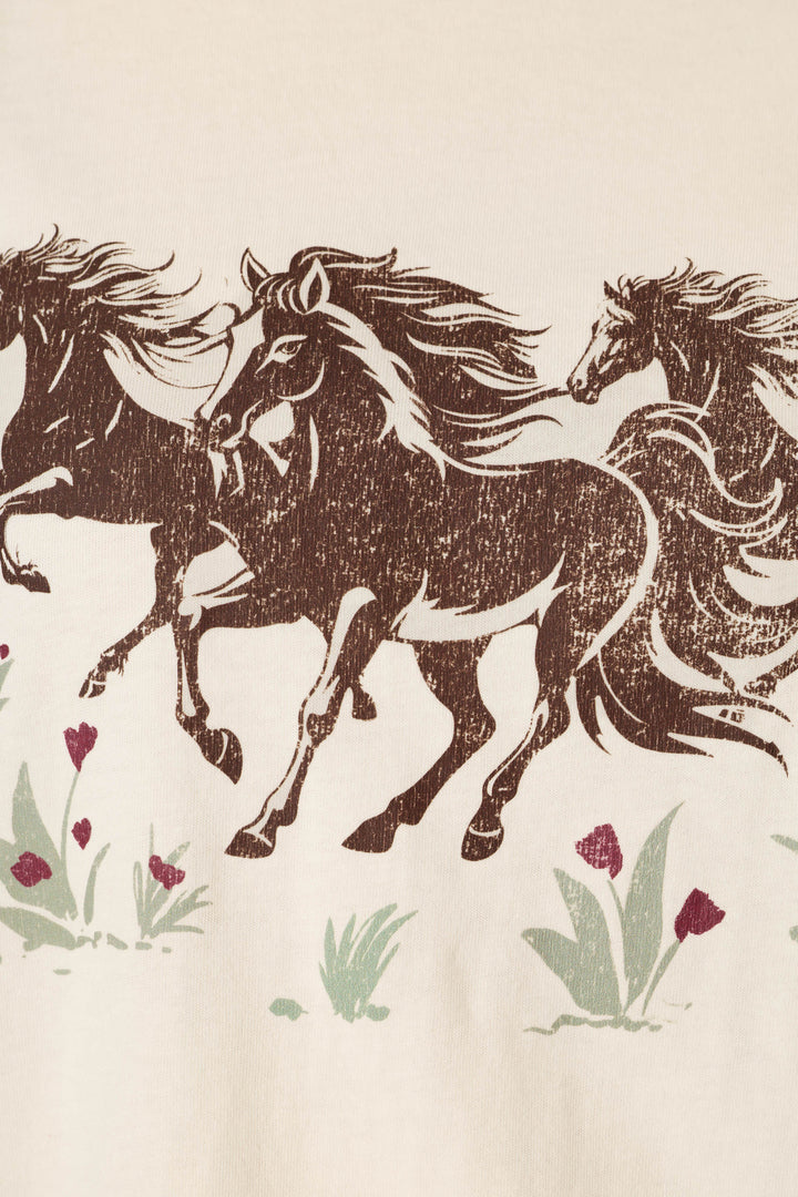 Introducing the P.J. Salvage Western Ways Wild Horses Graphic Shuggie T-Shirt, featuring an illustration of three brown horses with flowing manes running through green grass dotted with small red flowers, all set against a beige background.