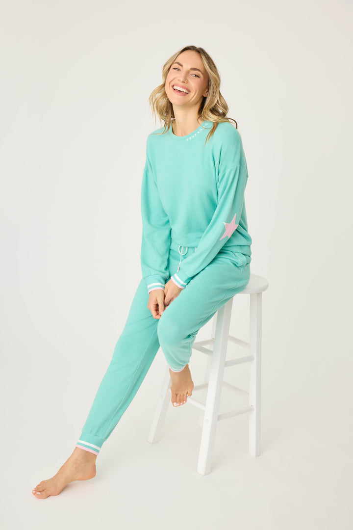 Teal green lounge set for women. Top has pink star print on elbows, pant has pockets with scallop-edging detail. Striped banded cuffs on top & pant.