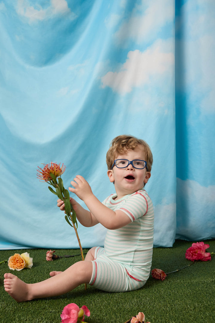 Gender-neutral kids' pajama in mint-ivory stripes with contrast red stitching.