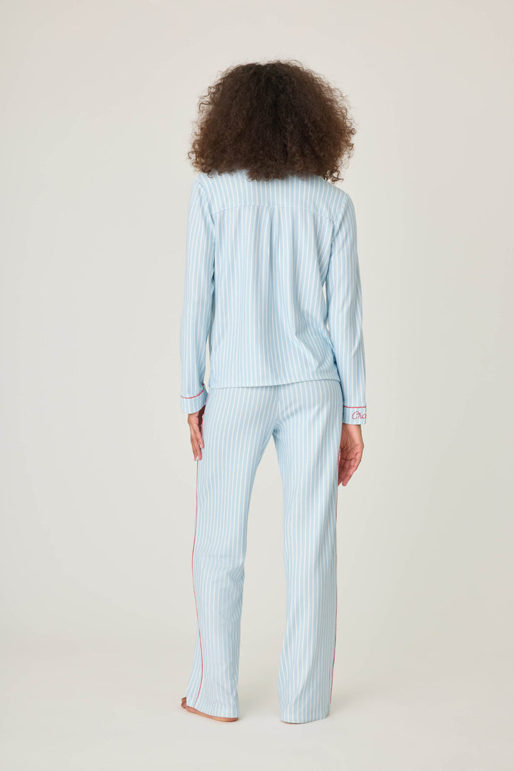 Women's classic pajama set in light blue-white striped butter jersey. Red piping at button-front top & sideseams of pant. Chest pocket with embroidered crab & matching sleep mask with 'Crabby' lettering.